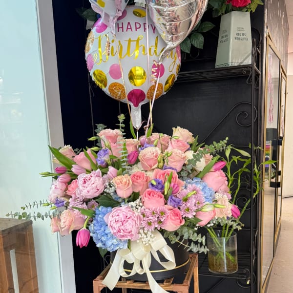 Pink and blue mixed flower arrangement in a black box with birthday balloons