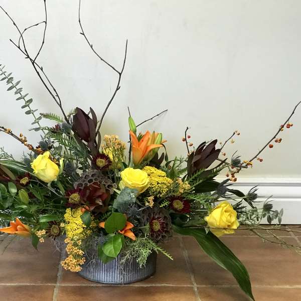 Low floral arrangement with yellow roses and orange lilies in a gray container