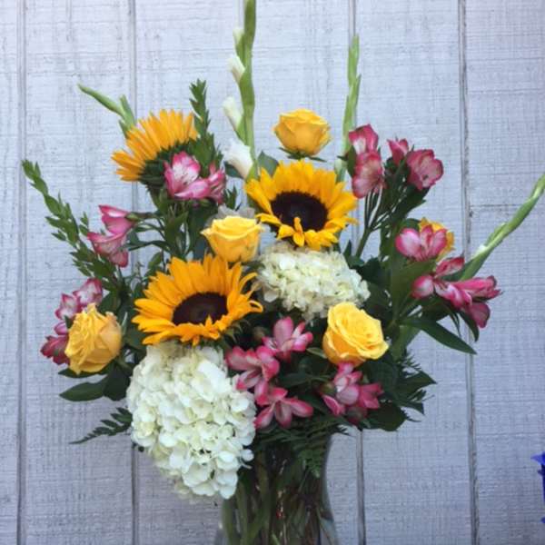 Bouquet of sunflowers, yellow roses, white hydrangeas, and pink alstroemeria in a glass vase