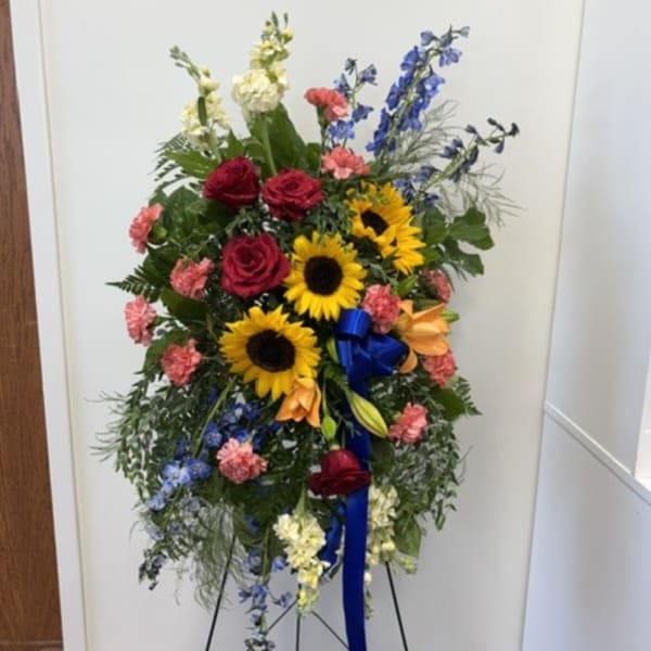 Standing floral spray with sunflowers, red roses, and blue flowers on an easel
