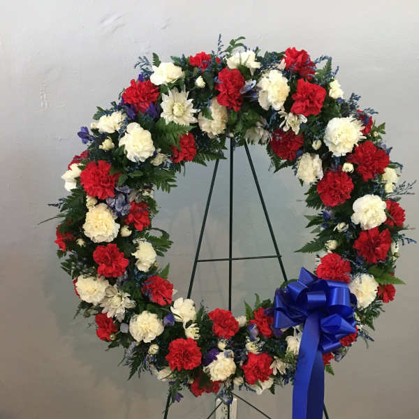 Circular wreath of red, white, and blue flowers on a stand with a blue bow