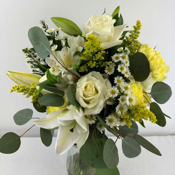 White roses and lilies in a glass vase with yellow filler flowers