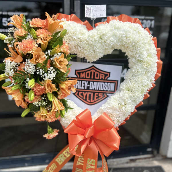 Heart-shaped floral tribute with white and orange flowers and a large orange bow
