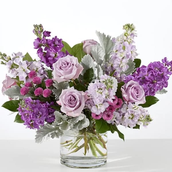 Lavender roses and purple flowers arranged in a clear glass vase