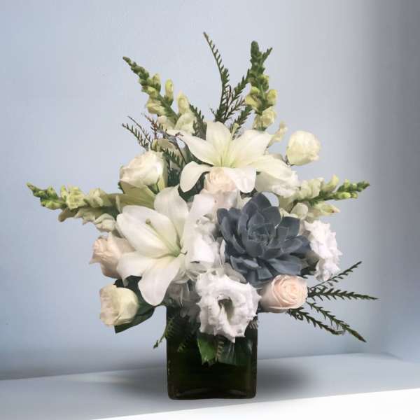 White lilies and roses arranged in a dark glass vase with a blue succulent