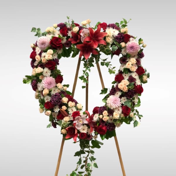 Heart-shaped floral wreath on a wooden stand with red, pink, and white flowers