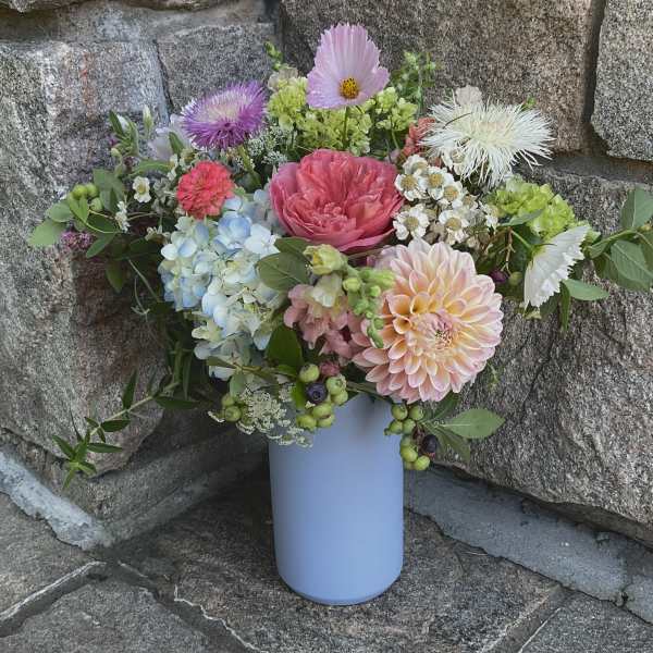 Mixed bouquet in a light blue vase with pink, peach, blue, and white blooms