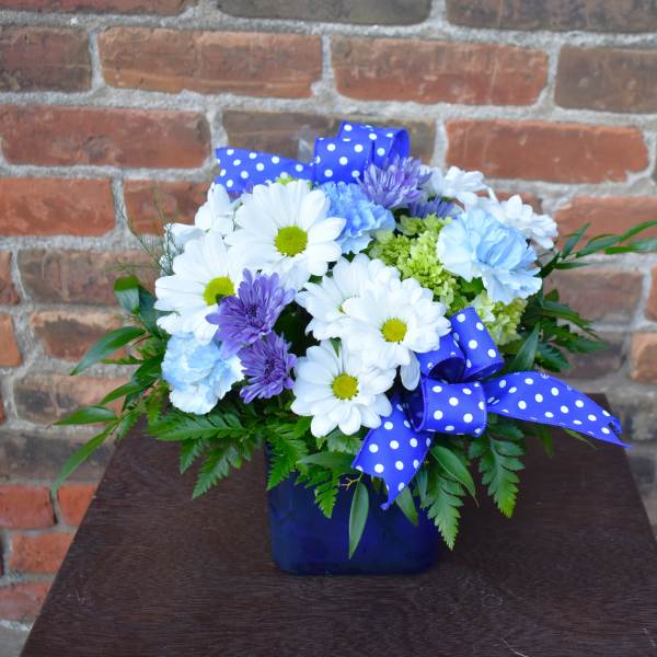 Blue vase arrangement with white daisies, purple blooms, and polka-dot ribbon