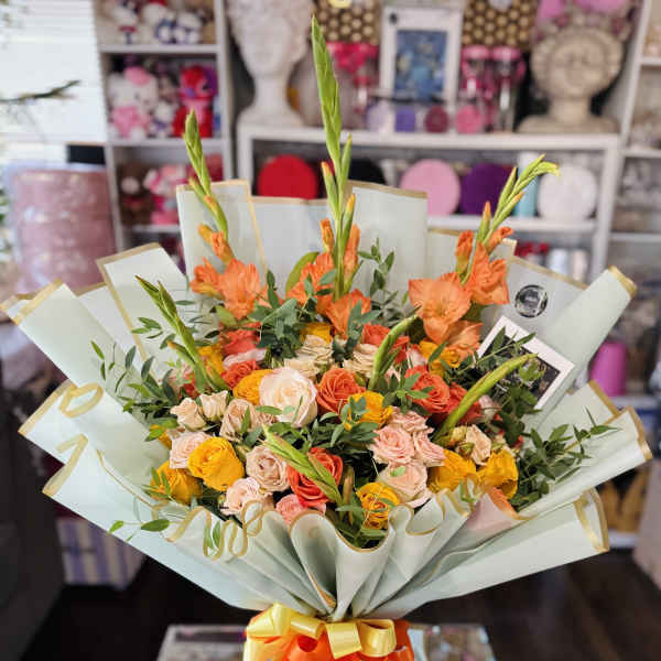 Bouquet of orange and peach roses with tall orange blooms wrapped in pale paper