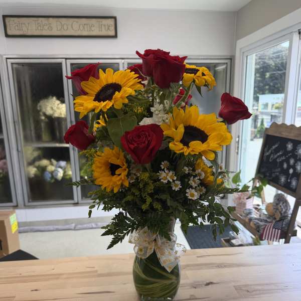 Red roses and yellow sunflowers in a glass vase with a ribbon