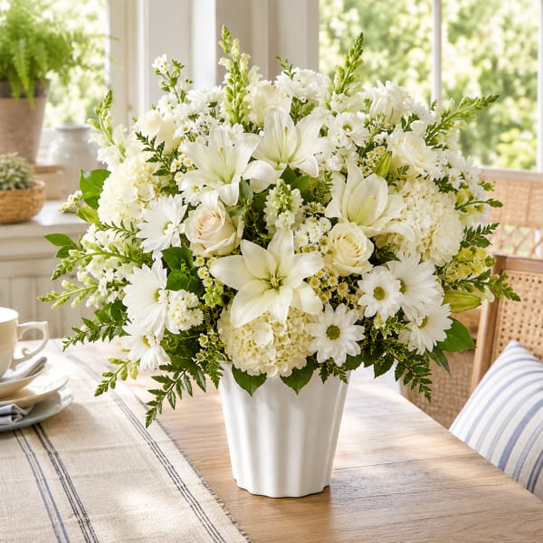 White floral arrangement in a white vase with lilies, roses, and daisies