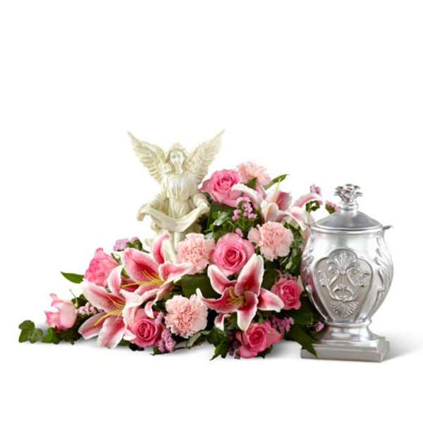Pink floral arrangement with lilies, roses, and an angel figurine beside a silver urn