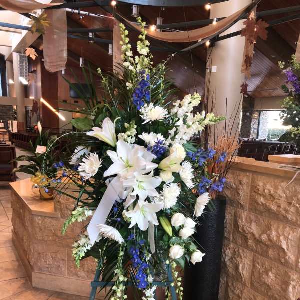 Tall white floral standing arrangement with blue accents on an easel