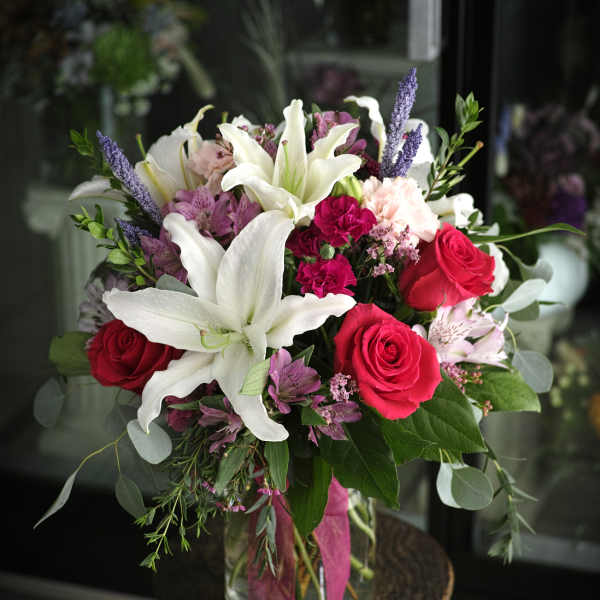 Bouquet of white lilies, red roses, and pink flowers in a glass vase