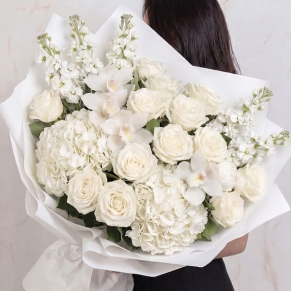 White bouquet of roses, orchids, and hydrangeas wrapped in paper