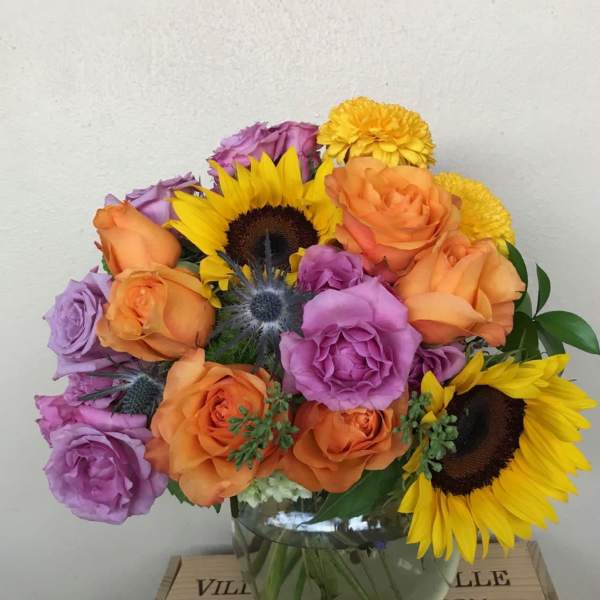 Bouquet of orange and purple roses with sunflowers in a glass vase