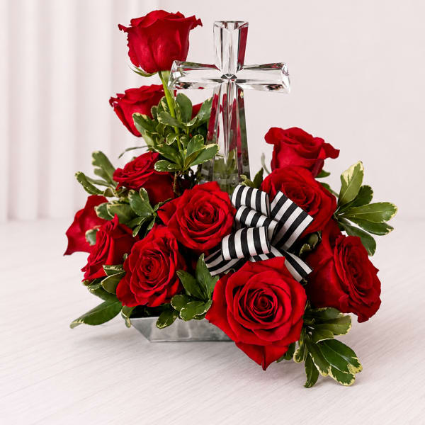 Red roses arranged around a clear glass cross with a striped ribbon