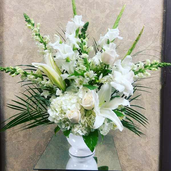 White floral arrangement in a white vase with lilies and roses