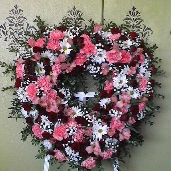 Heart-shaped floral wreath on an easel with pink, white, and red flowers