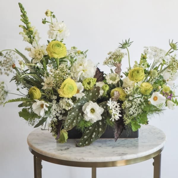 Low floral arrangement with yellow and white blooms in a black container
