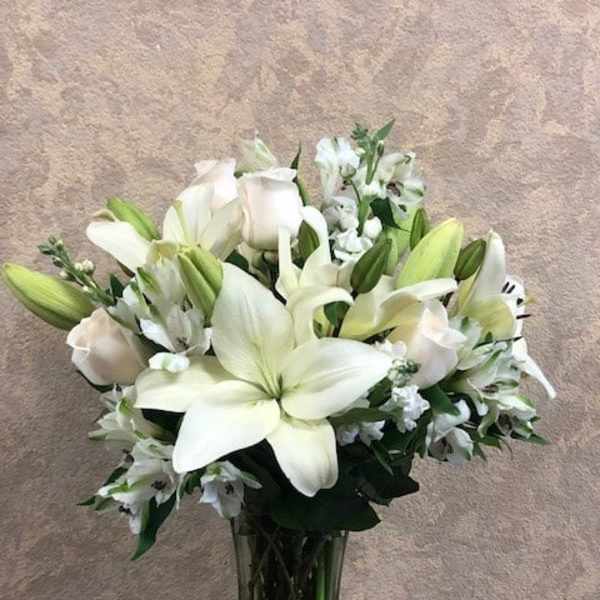 White lilies and roses arranged in a clear glass vase