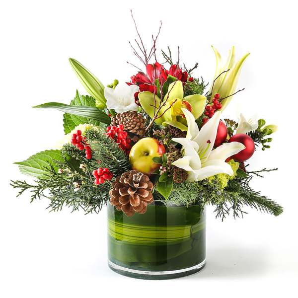 Holiday bouquet with lilies, apples, berries, and pinecones in a green glass vase