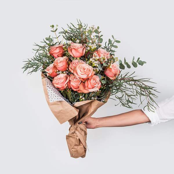 Hand-tied bouquet of peach roses with airy greenery and brown paper wrap