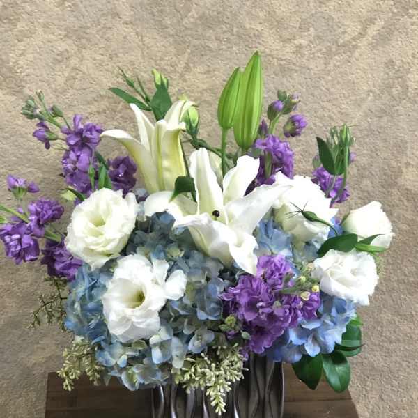 White lilies and blue hydrangeas with purple flowers in a dark vase