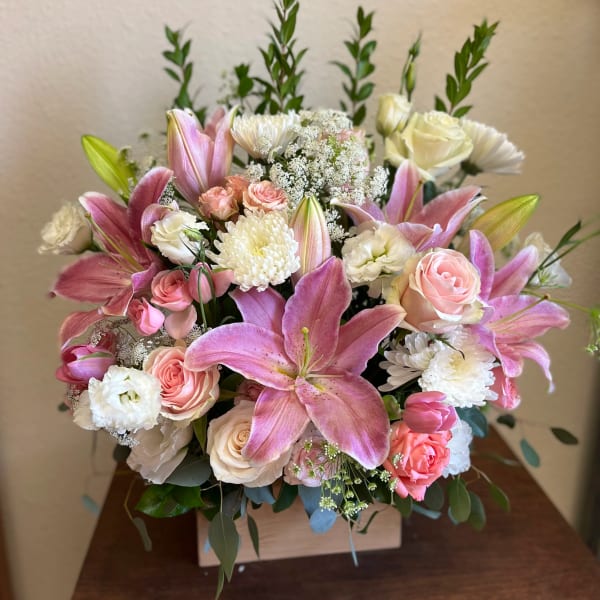 Pink lilies and roses arranged in a square wooden box