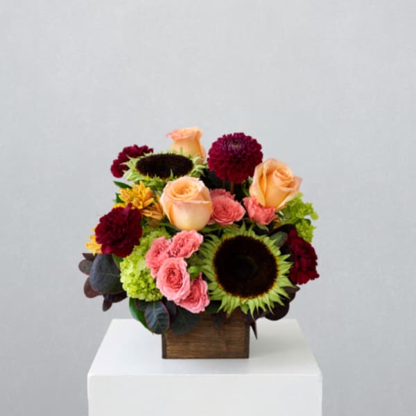 Mixed bouquet in a wooden box with peach roses, sunflowers, and burgundy blooms