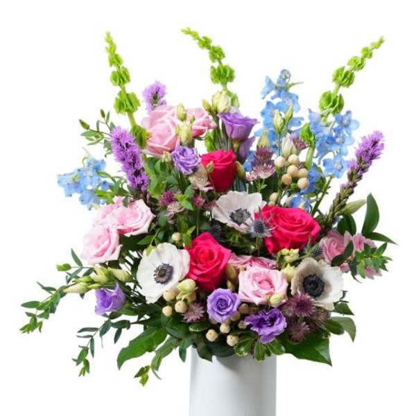 Tall mixed bouquet of pink roses, white anemones, and purple and blue blooms in a white vase