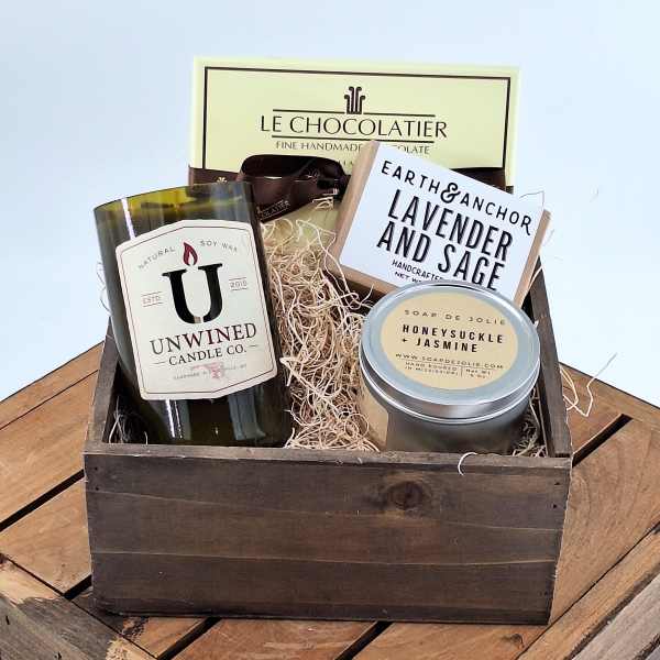 Gift basket with a candle, soap, chocolate, and a tin container in a wooden crate