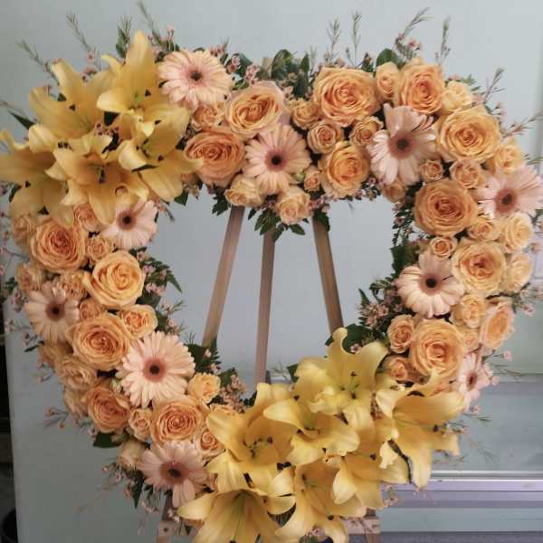 Heart-shaped floral wreath with peach roses, pink daisies, and yellow lilies