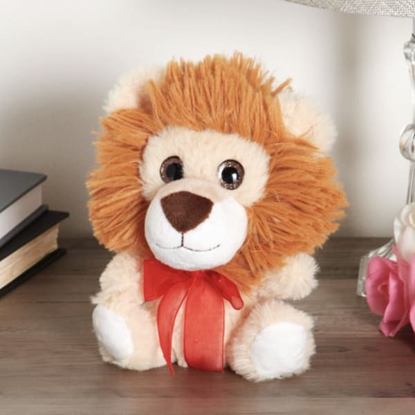 Plush lion toy with a red ribbon bow sitting on a table