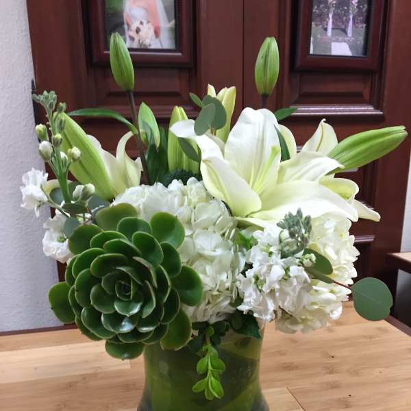 White lilies and hydrangeas in a green glass vase with succulents.