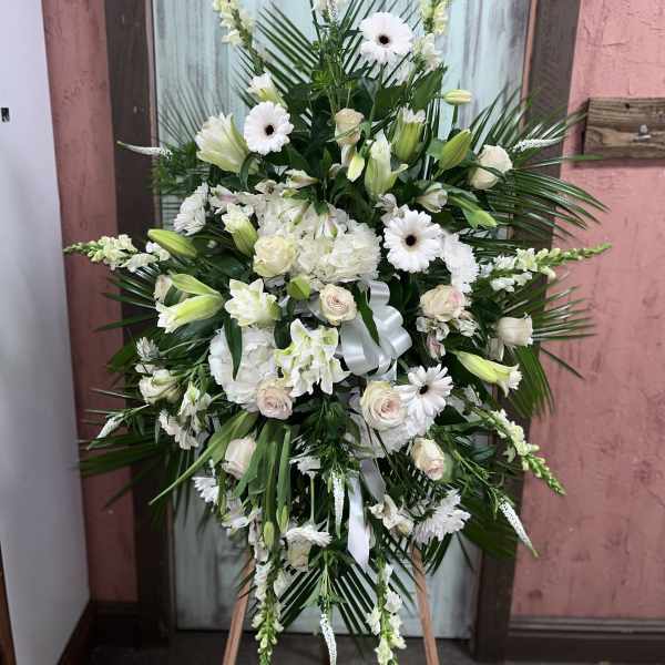 Large white funeral spray with lilies, roses, and daisies on an easel