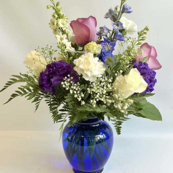 Mixed bouquet in a blue glass vase with pink, purple, white, and yellow flowers