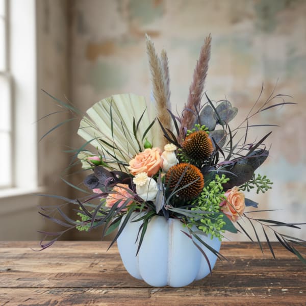 Peach roses in a white pumpkin-shaped vase with dried grasses and dark foliage