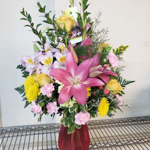 Mixed bouquet with pink lilies, yellow roses, and pink carnations in a burgundy vase