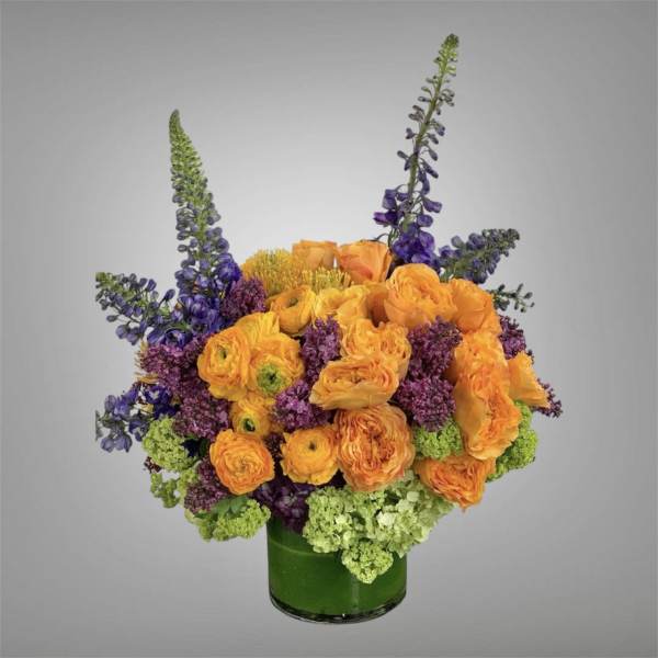 Orange and purple mixed bouquet in a green glass vase