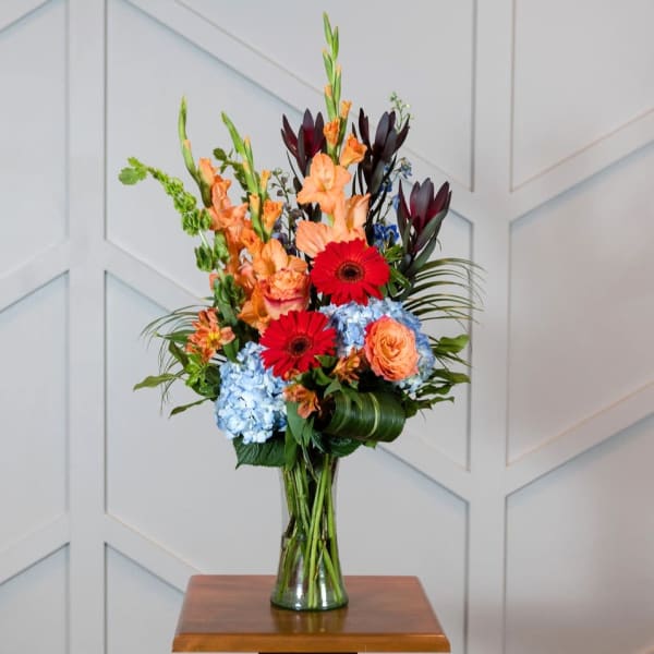Tall bouquet of orange, red, and blue flowers in a glass vase