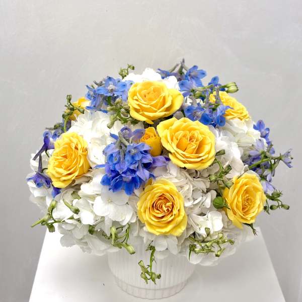 Yellow roses and blue flowers arranged in a white vase