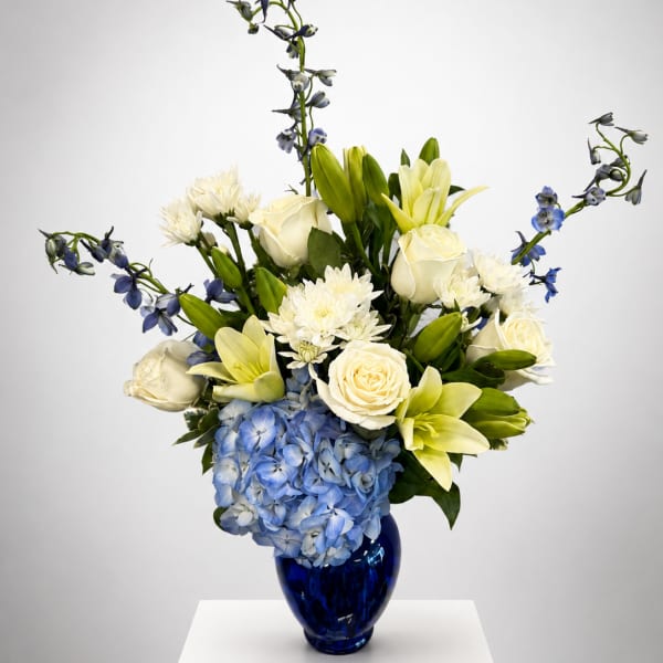 Blue hydrangeas, white roses, lilies, and blue delphinium in a cobalt vase