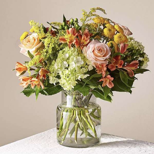 Mixed bouquet of roses, hydrangeas, and orange lilies in a glass vase