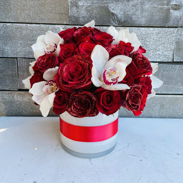 Red roses and white orchids in a white hat box with a red ribbon