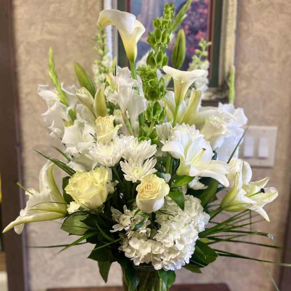 White floral arrangement in a clear glass vase with lilies, roses, and hydrangea