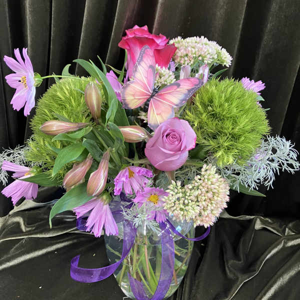 Pink and lavender floral arrangement in a glass vase with a butterfly accent