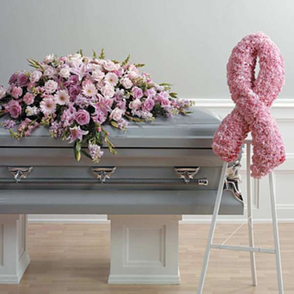 Pink floral casket spray on a gray casket beside a pink ribbon wreath