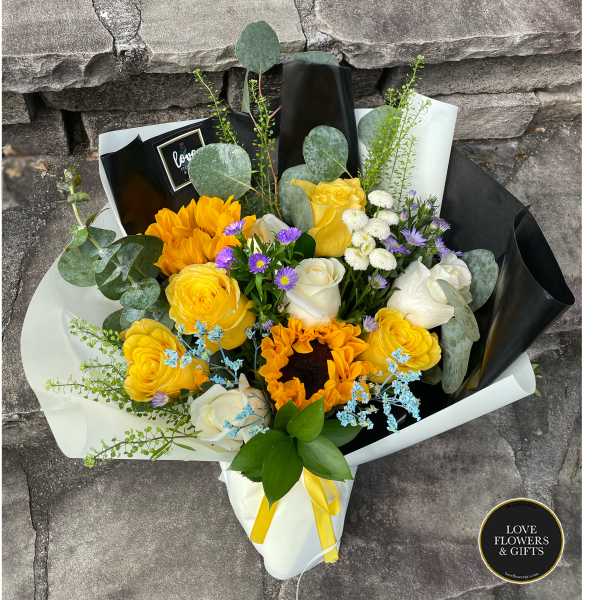 Hand-tied bouquet with sunflowers, yellow and white roses, and purple asters in paper wrap
