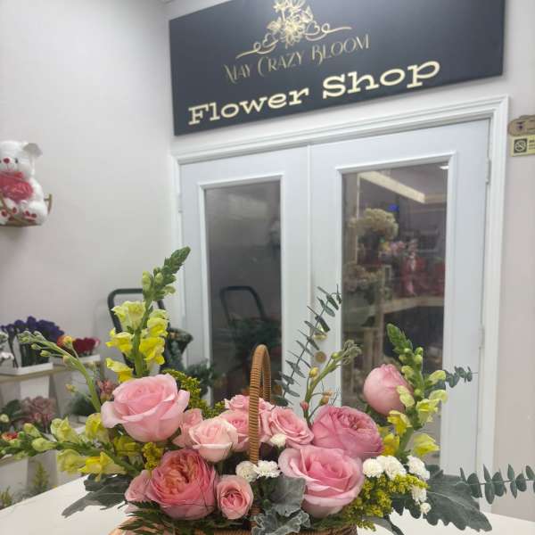 Pink roses and yellow snapdragons in a wicker basket with ribbon